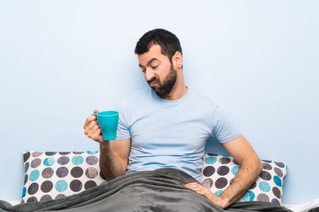 Man in bed with beard holding a cup of coffeeの写真素材
