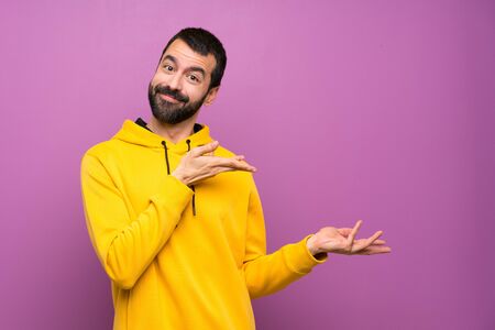 Handsome man with yellow sweatshirt extending hands to the side for inviting to comeの写真素材