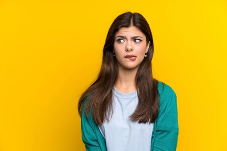 Teenager girl over yellow wall having doubts and with confuse face expressionの写真素材