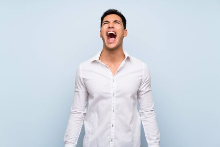 Handsome man over blue wall shouting to the front with mouth wide openの写真素材