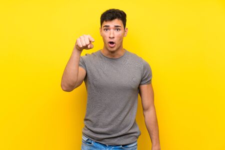 Handsome man over isolated yellow wall surprised and pointing frontの写真素材