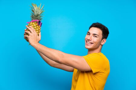 Handsome man over blue background holding a pineapple with sunglasseの写真素材