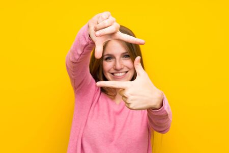Young woman with long hair over isolated yellow wall focusing face. Framing symbol