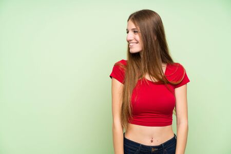 Young woman with long hair over isolated green wall standing and looking to the sideの写真素材