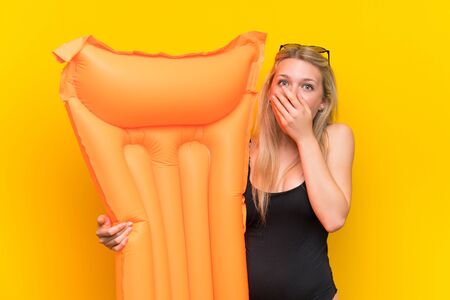 Young woman in swimsuit over yellow background covering mouth with handsの写真素材