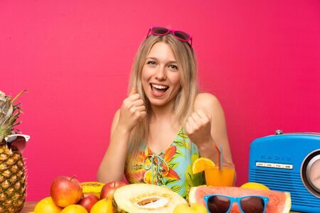 Young blonde woman with lots of fruits celebrating a victoryの写真素材