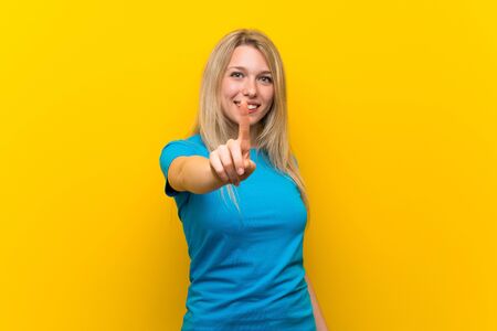 Young blonde woman over isolated yellow background showing and lifting a fingerの写真素材