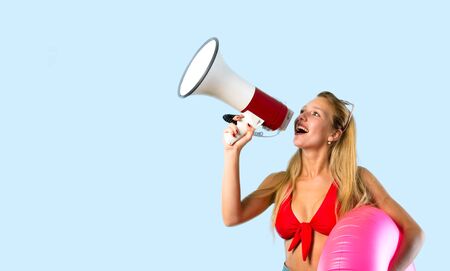 Blonde woman in summer vacation holding a megaphone on blue backgroundの写真素材