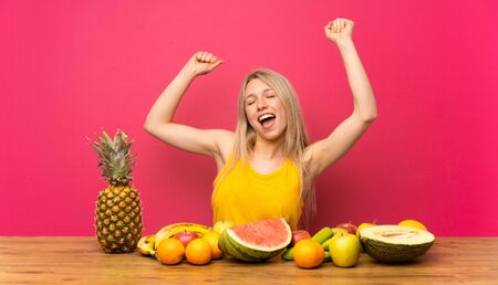 Young blonde woman with lots of fruits celebrating a victoryの写真素材