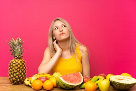 Young blonde woman with lots of fruits thinking an ideaの写真素材