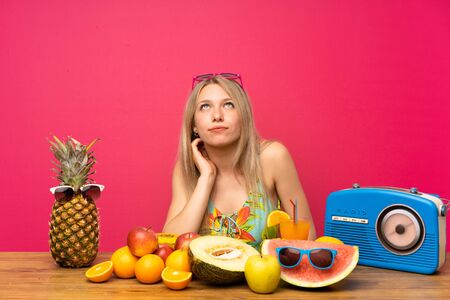 Young blonde woman with lots of fruits thinking an ideaの写真素材