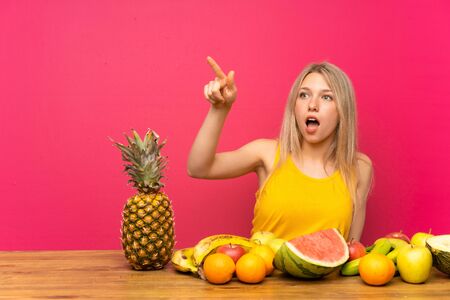 Young blonde woman with lots of fruits pointing awayの写真素材