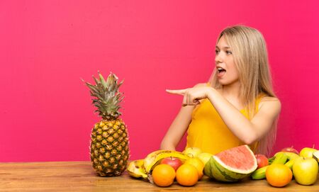Young blonde woman with lots of fruits pointing finger to the sideの写真素材