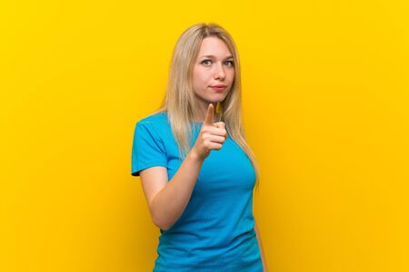 Young blonde woman over isolated yellow background frustrated and pointing to the frontの写真素材