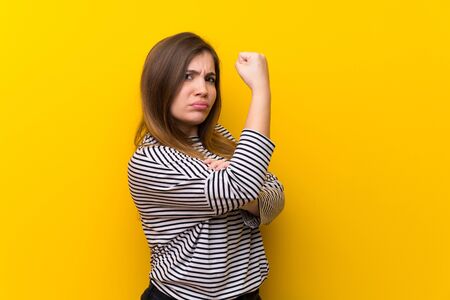 Young girl over yellow wall doing strong gestureの写真素材