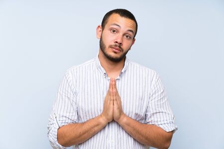 Colombian man over isolated blue wall keeps palm together. Person asks for somethingの写真素材