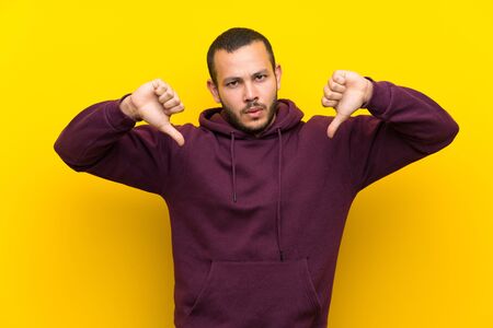 Colombian man with sweatshirt over yellow wall showing thumb downの写真素材