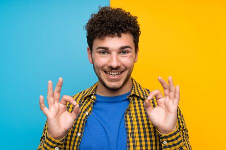 Man with curly hair over colorful wall showing an ok sign with fingersの写真素材
