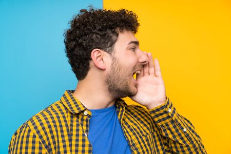 Man with curly hair over colorful wall shouting with mouth wide openの写真素材