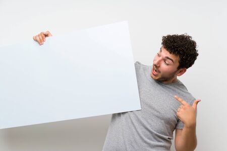 Man with curly hair over isolated wall holding an empty white placard for insert a conceptの写真素材