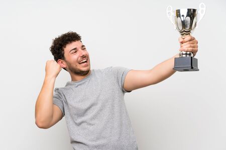 Man with curly hair over isolated wall holding a trophyの写真素材