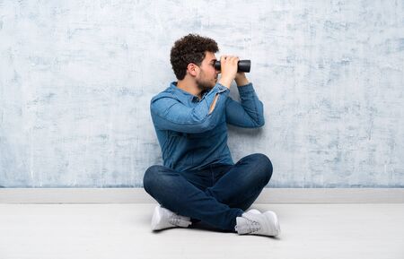 Young man sitting on the floor with black binocularsの写真素材