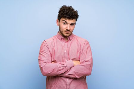 Man with curly hair over isolated blue wall feeling upsetの写真素材
