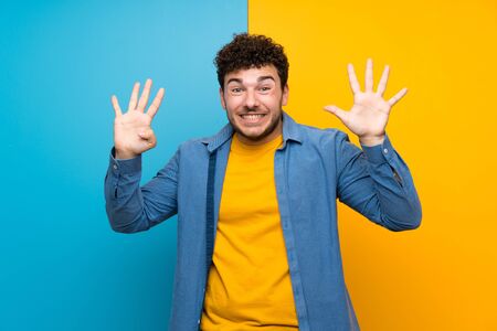 Man with curly hair over colorful wall counting nine with fingersの写真素材
