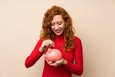 Redhead woman with turtleneck sweater holding a big piggybankの写真素材