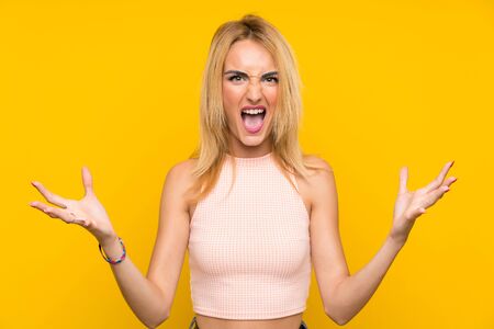 Young blonde woman over isolated yellow wall unhappy and frustrated with somethingの写真素材