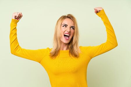 Young blonde woman over isolated green background celebrating a victoryの写真素材