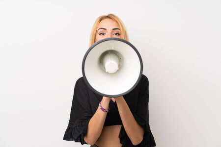 Young blonde woman over isolated white wall shouting through a megaphoneの写真素材