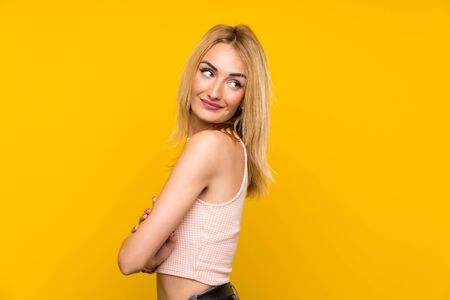 Young blonde woman over isolated yellow wall laughingの写真素材