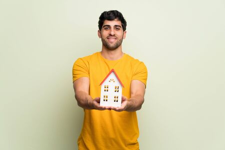 Young man over pink wall holding a little houseの写真素材