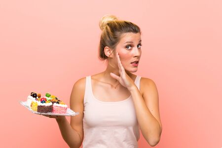 Young blonde woman holding lots of different mini cakes whispering somethingの写真素材