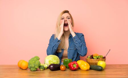 Young blonde woman with many vegetables shouting and announcing somethingの写真素材