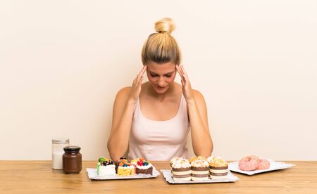 Young woman with lots of different mini cakes in a table unhappy and frustrated with something. Negative facial expressionの写真素材