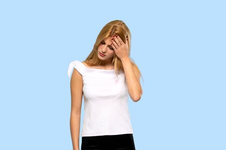 Young blonde woman with tired and sick expression on isolated blue backgroundの写真素材