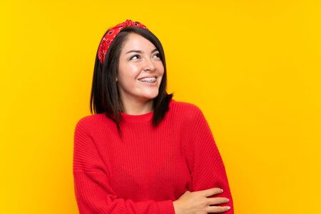 Young Mexican woman with red sweater over yellow wall laughingの写真素材