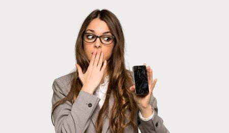 Business woman with troubled holding broken smartphone over isolated grey background