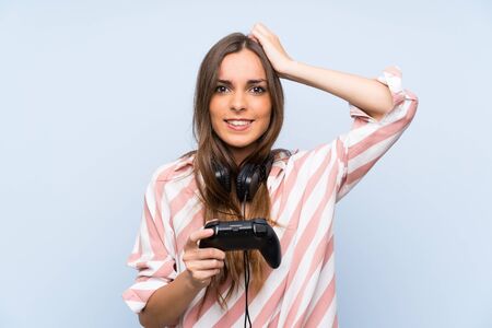 Young woman playing with a video game controller over isolated blue wallの写真素材