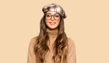 Young woman with beret with glasses and happy over isolated yellow backgroundの写真素材
