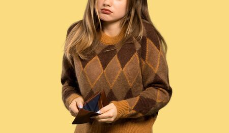 Teenager girl with brown sweater holding a wallet over isolated yellow background