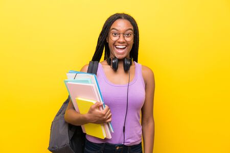 African American teenager student girl with long braided hair over isolated yellow wall with surprise facial expressionの写真素材