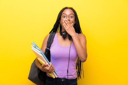 African American teenager student girl with long braided hair over isolated yellow wall with surprise facial expressionの写真素材