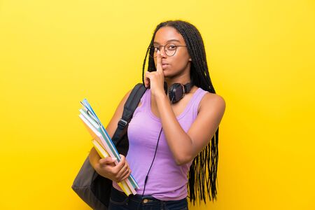 African American teenager student girl with long braided hair over isolated yellow wall doing silence gestureの写真素材