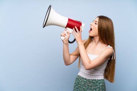 Young woman over isolated blue background shouting through a megaphoneの写真素材
