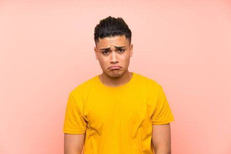 Young man with yellow shirt over isolated pink wall sad