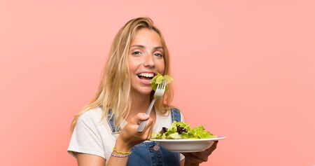 Happy Blonde young woman with salad over isolated pink wallの写真素材
