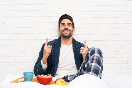 Man in bed with dressing gown and having breakfast pointing up a great ideaの写真素材